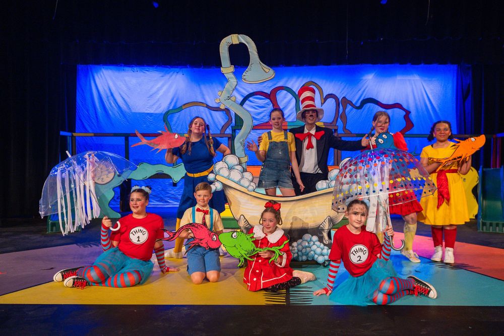 Colorful theatrical stage performance featuring performers in whimsical costumes and Dr. Seuss-inspired set pieces.