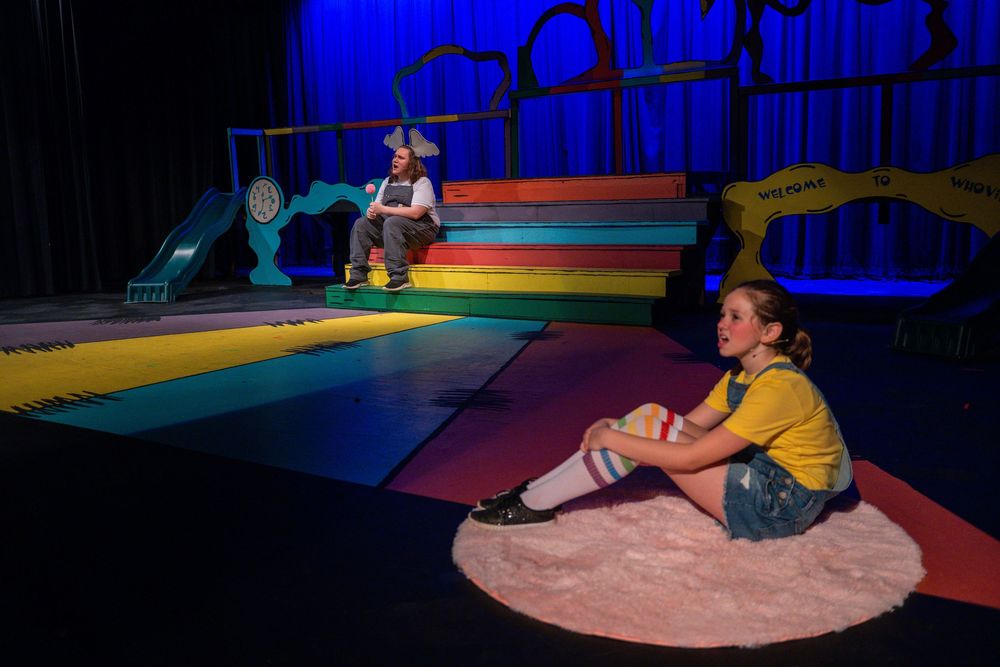 Performers reenact a whimsical scene from Dr. Seuss' Cat in the Hat on a colorful stage with dramatic blue lighting.