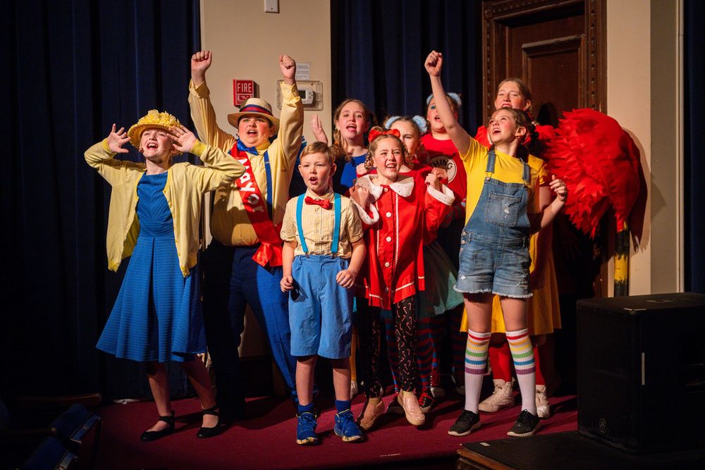 Performers in colorful costumes dance and pose together during a theatrical stage production.