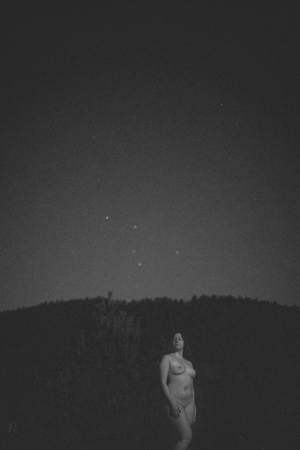 A silhouetted figure standing at night under a starlit sky with trees in the background.