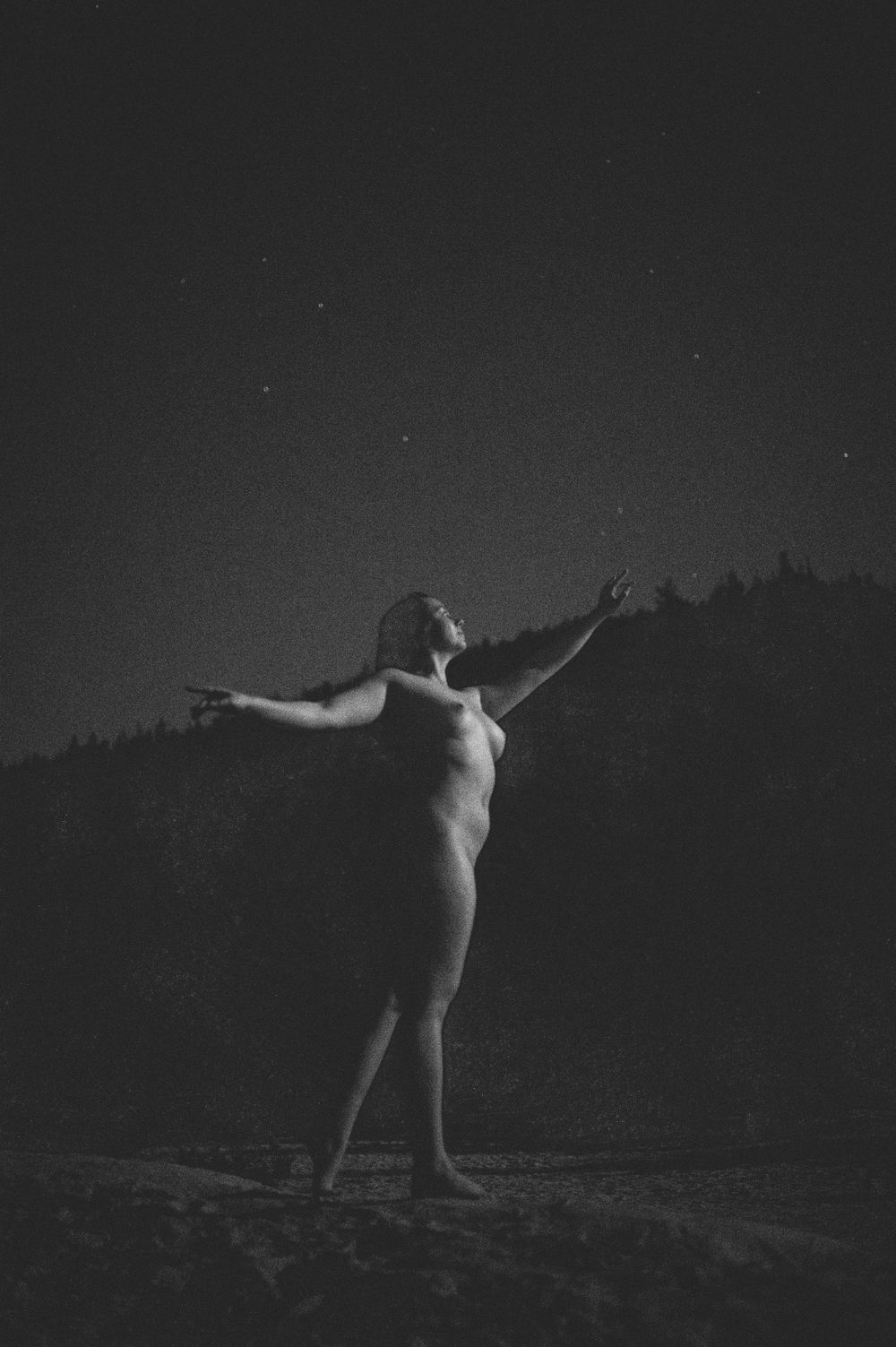 Black and white photo series of a person performing expressive dance movements in darkness against a night sky.