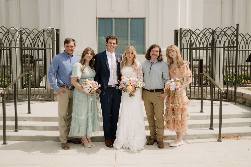 Wedding party poses together on white church steps with decorative iron railings and blue windows.
