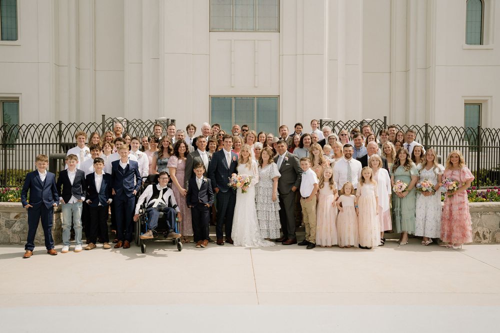 Large wedding group photo with entire party and guests posed outside white building.