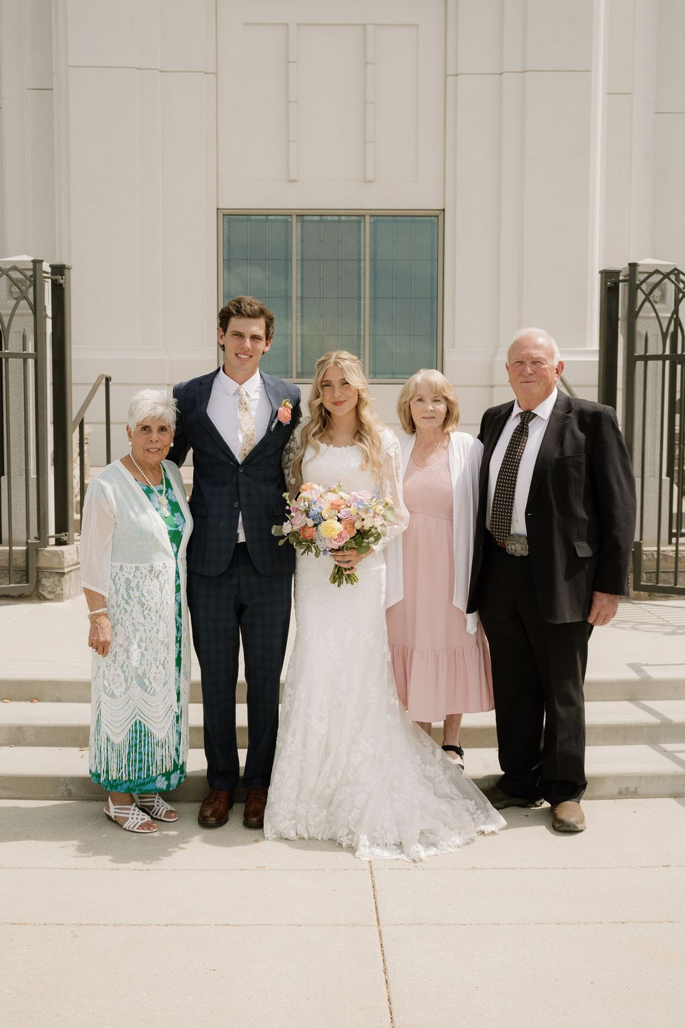 A group poses together on white church steps for a formal wedding photo.