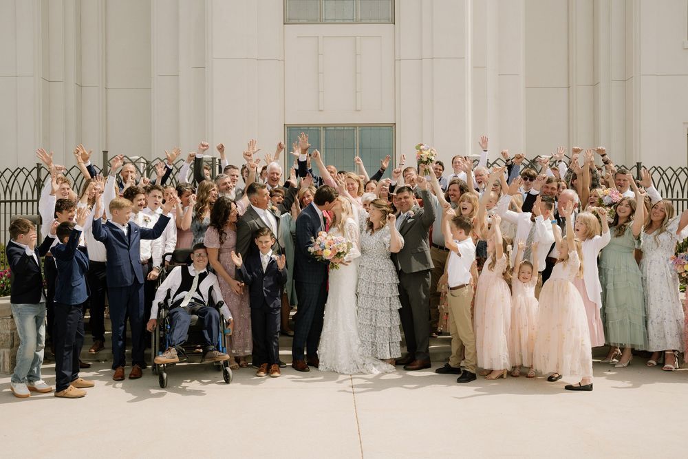 Large wedding group cheers and celebrates outside white church building.