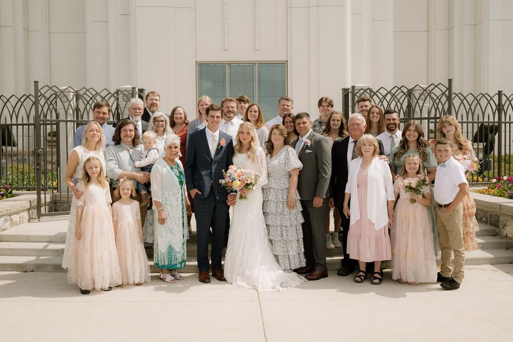 Large wedding party group photo with family members gathered outside a white church building.