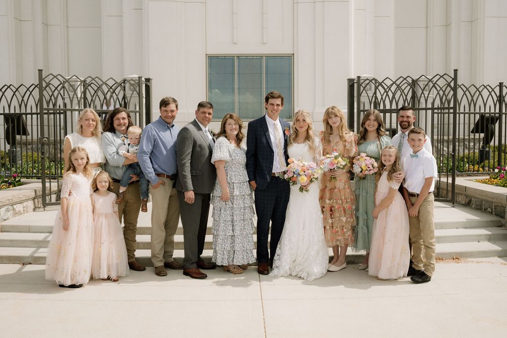 Small wedding party poses for formal portrait outside white church building with decorative iron fence.