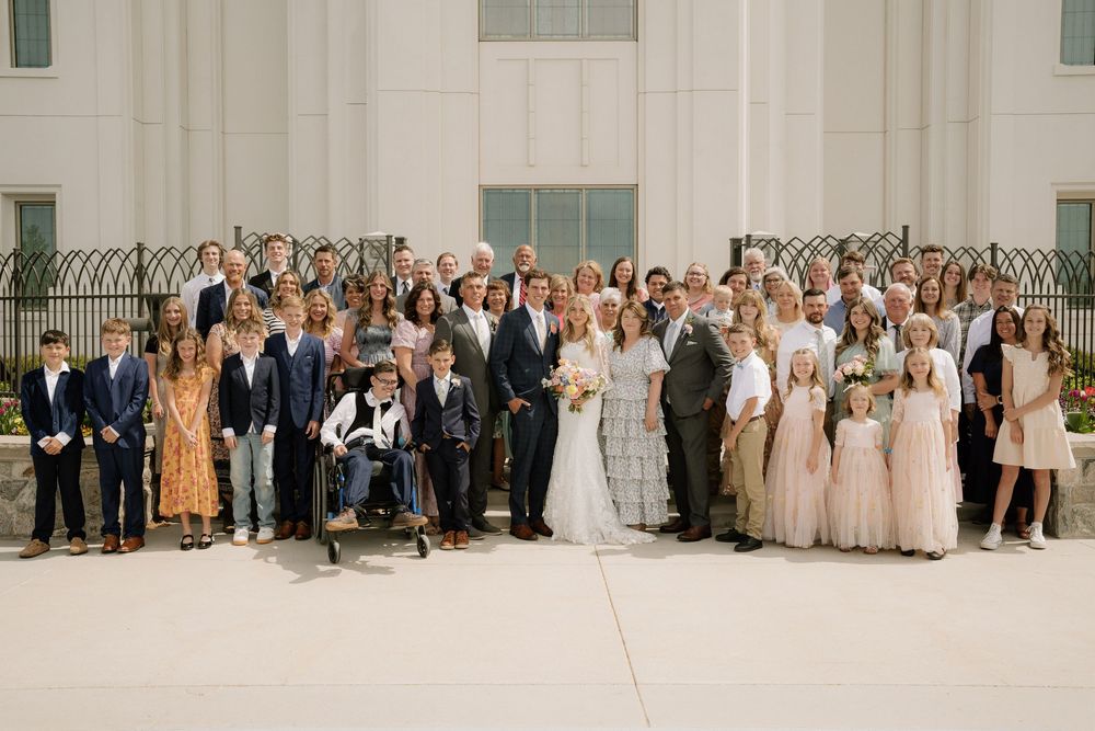Large wedding party group photo outside a white church building with the newlyweds in the center.