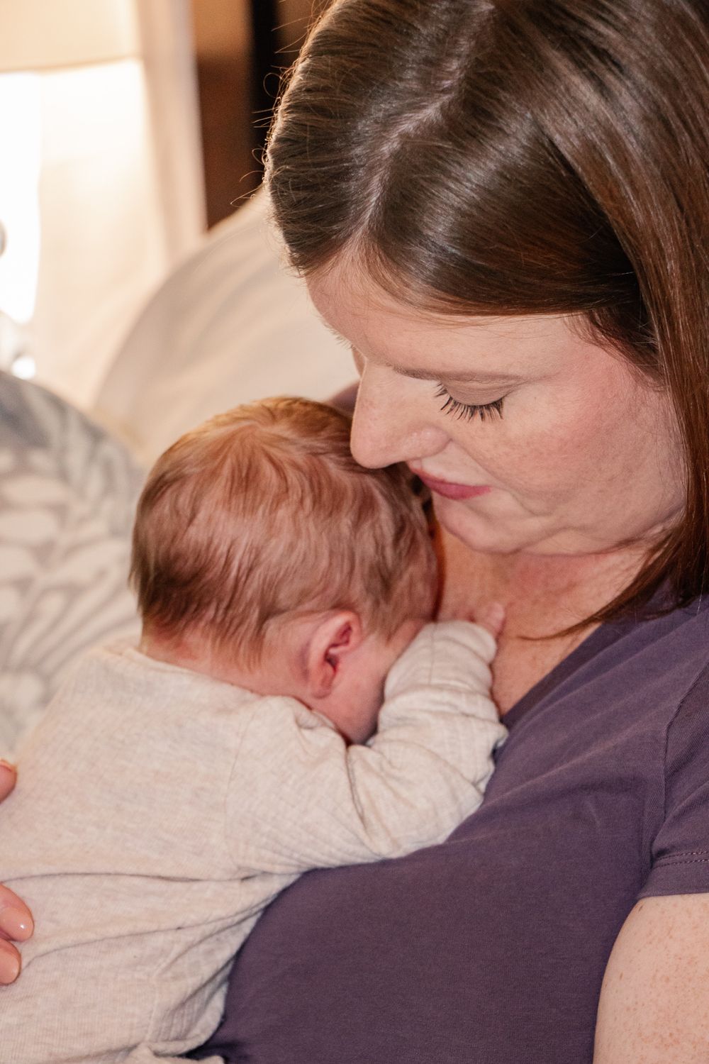 Mother gently resting her head over her newborn's as they snuggle close, capturing a quiet moment of bonding.