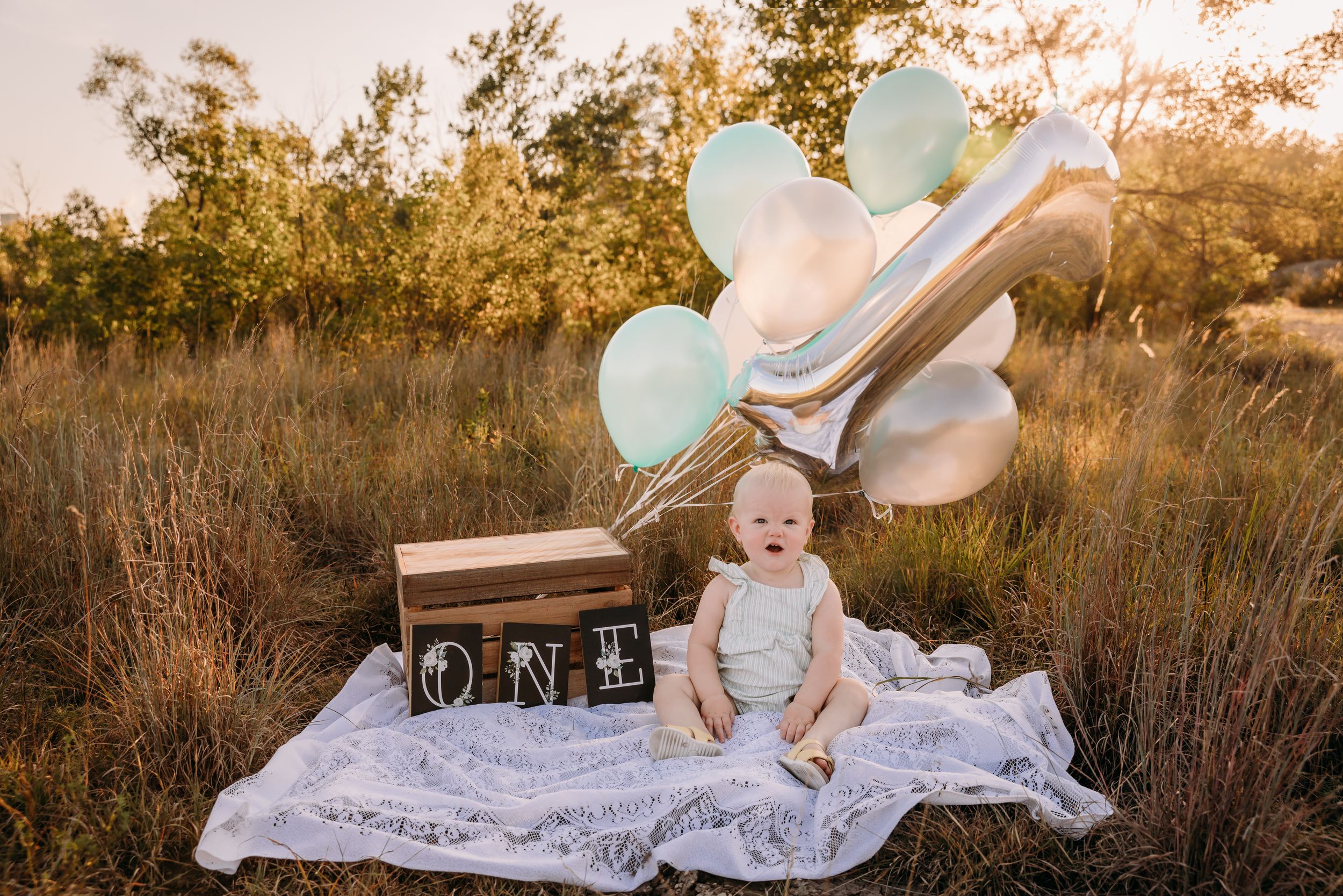 Baby sitting on white blanket outdoors during golden hour sunset.