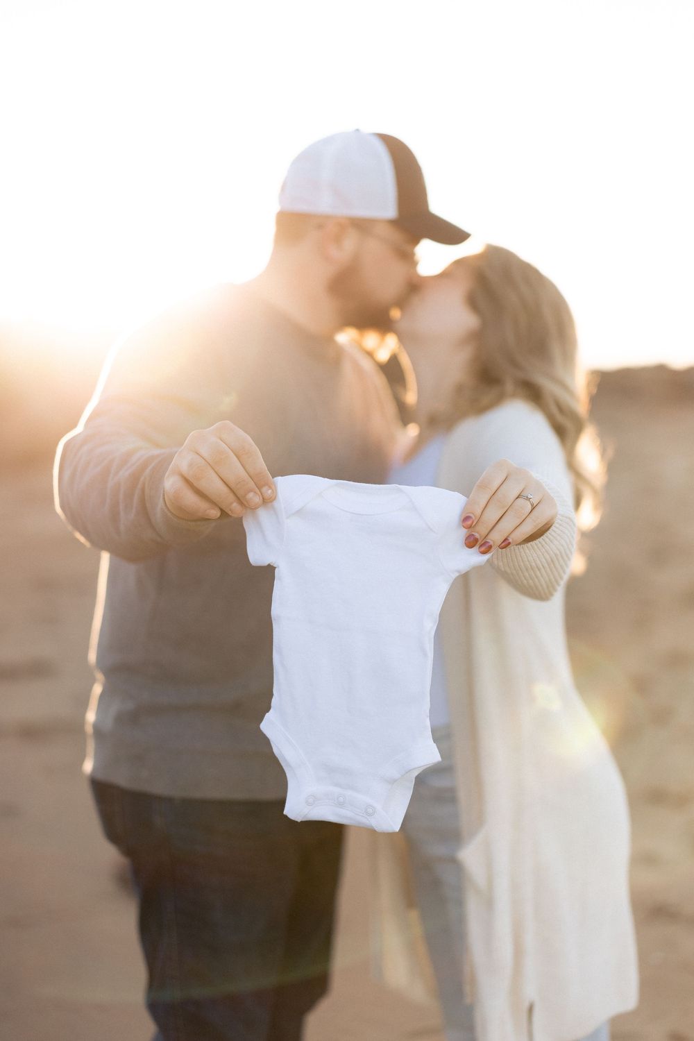 couple hold up onesie at sunset in Aboiteau beach in New Brunswick, Moncton maternity photographer, beach maternity session, pregnancy
