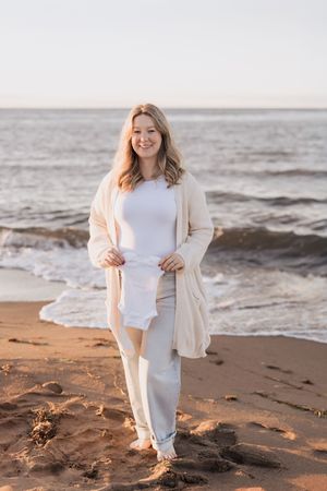 Mom holds baby onesie at sunset infront of the ocean, Shediac photographer maternity session, Parlee beach photographer vacation photos