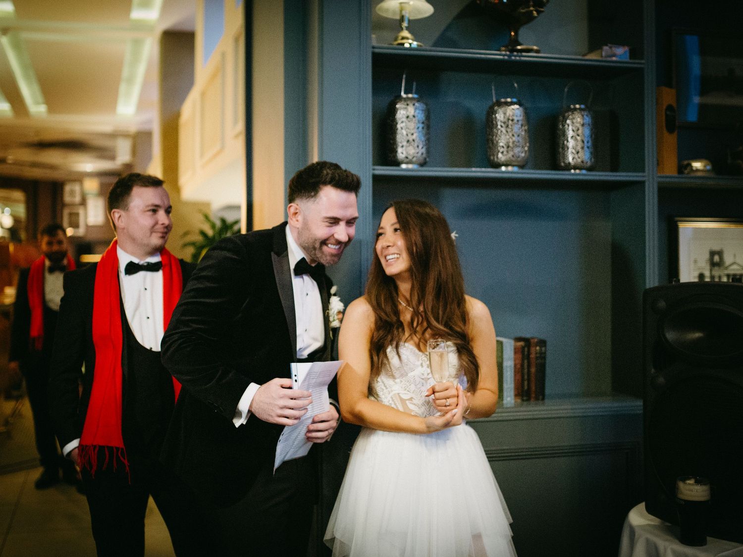 An elegant couple shares a laugh together at their wedding reception while dressed in formal attire near a bar.