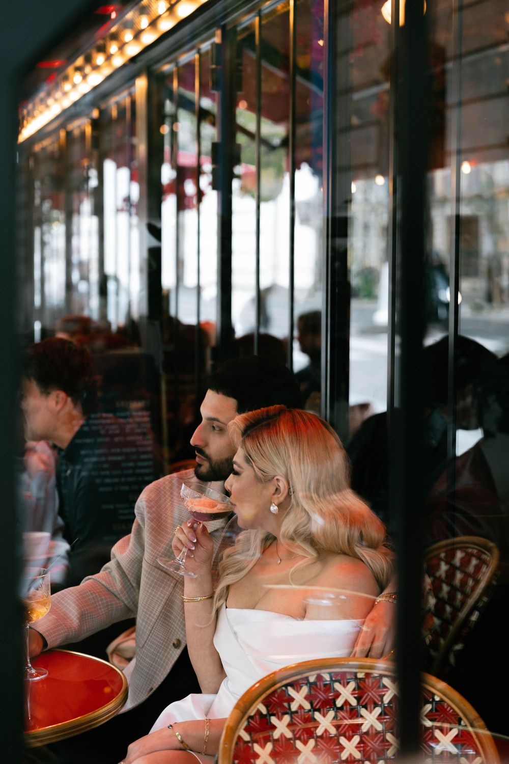 People dining at a dimly lit restaurant sit at wooden tables with bistro chairs by windows with reflective surfaces.
