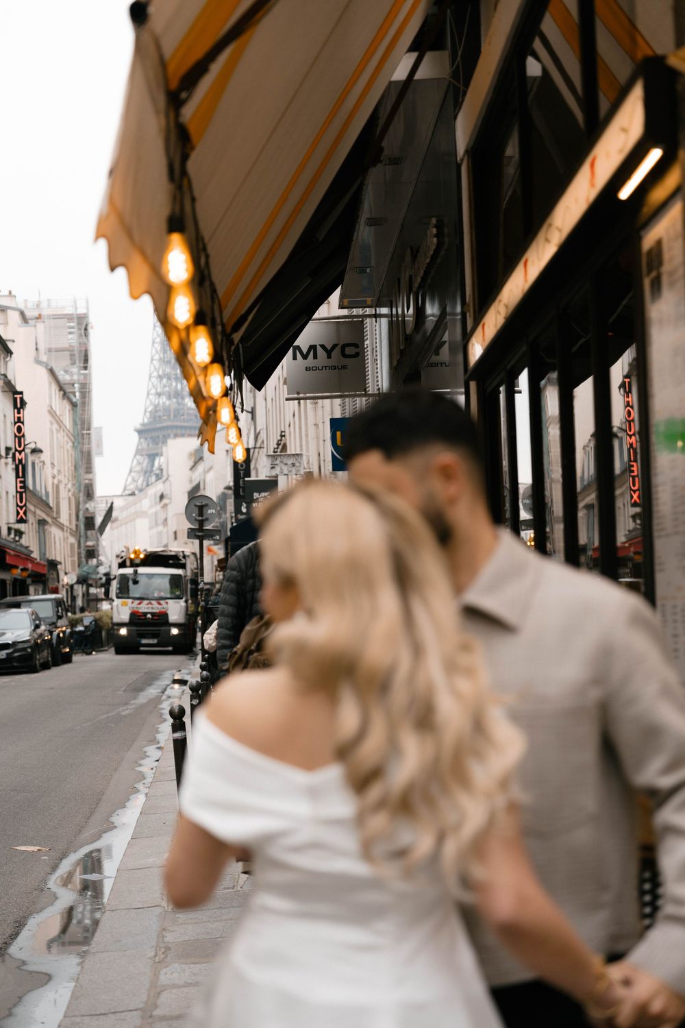 A romantic couple walking on a charming Parisian street with the iconic Eiffel Tower visible in the background.