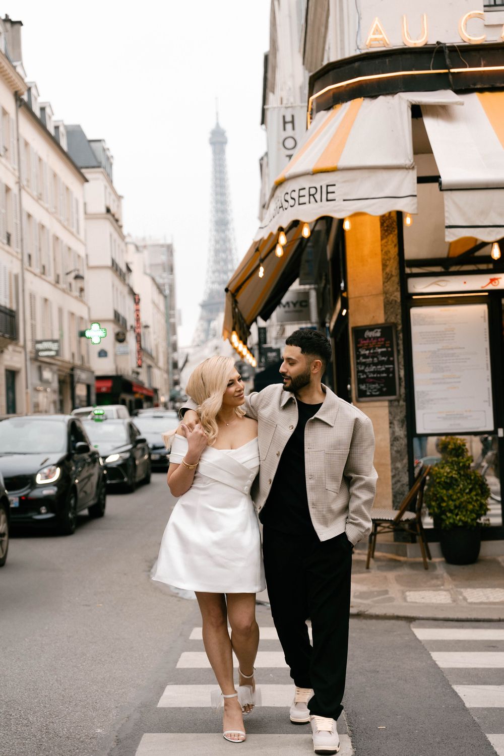 A couple shares a romantic moment on a Parisian corner street with the Eiffel Tower in view.