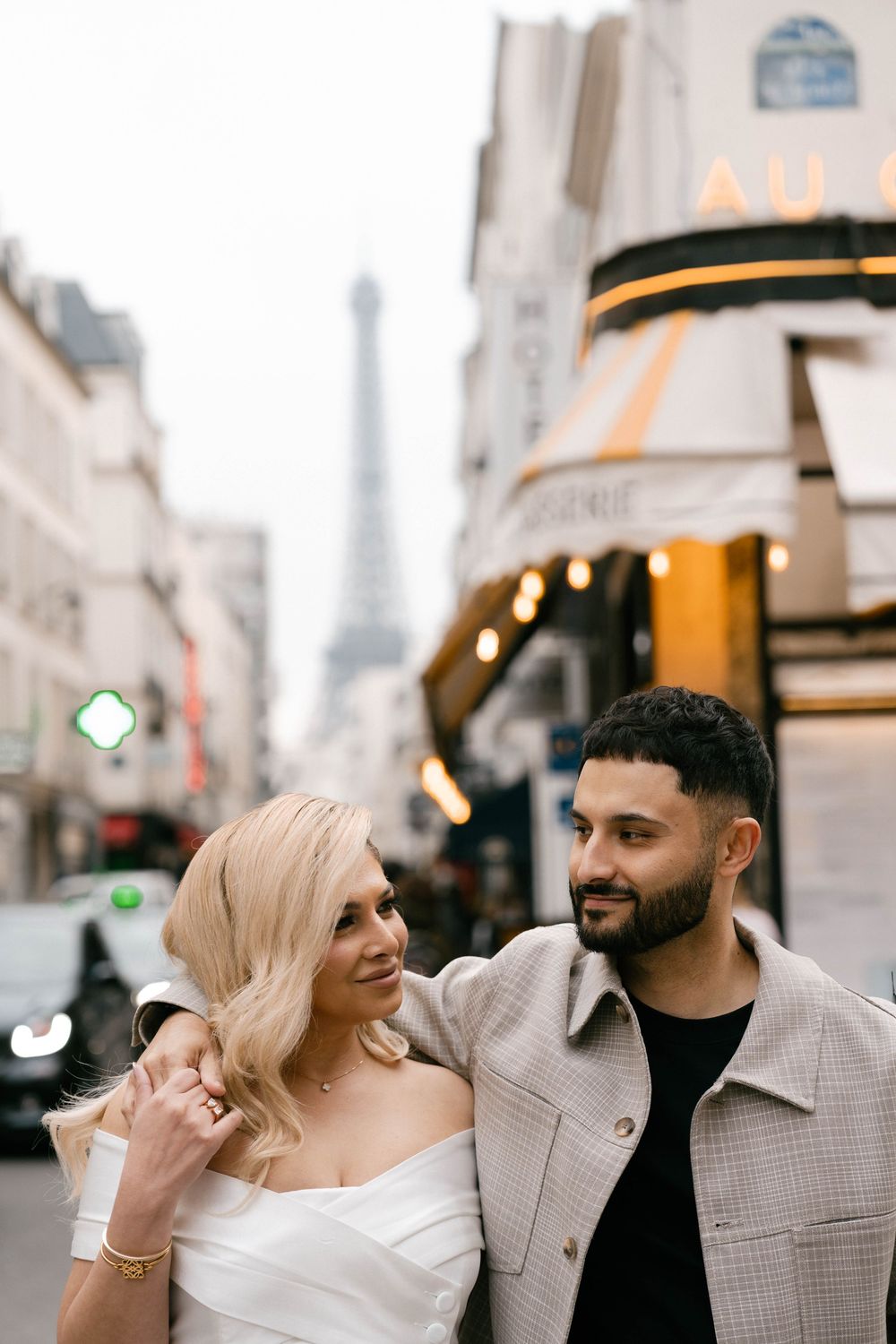A romantic couple shares a joyful moment on a charming Paris street with the Eiffel Tower visible in the background.