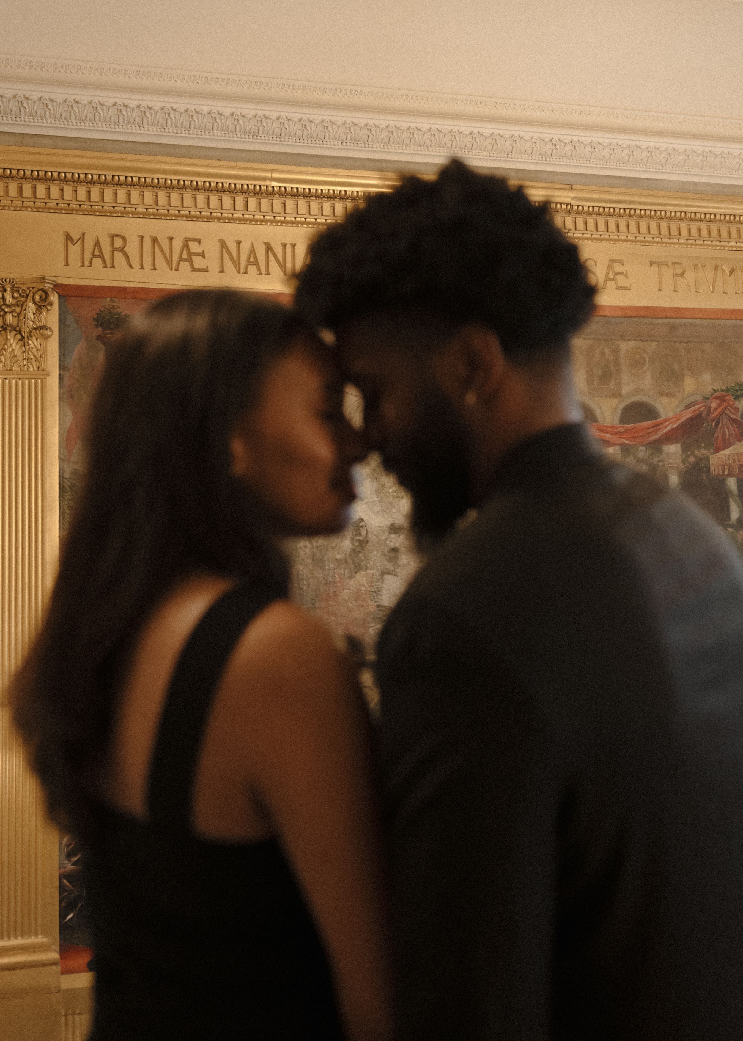 A couple sharing an intimate moment in silhouette against an ornate wall with classical architectural details.