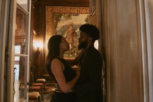 An intimate couple's portrait in a warmly lit hallway with ornate decor and artwork visible in the background.