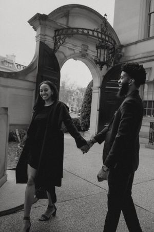 A joyful couple holding hands while walking under an architectural archway in black and white photography.