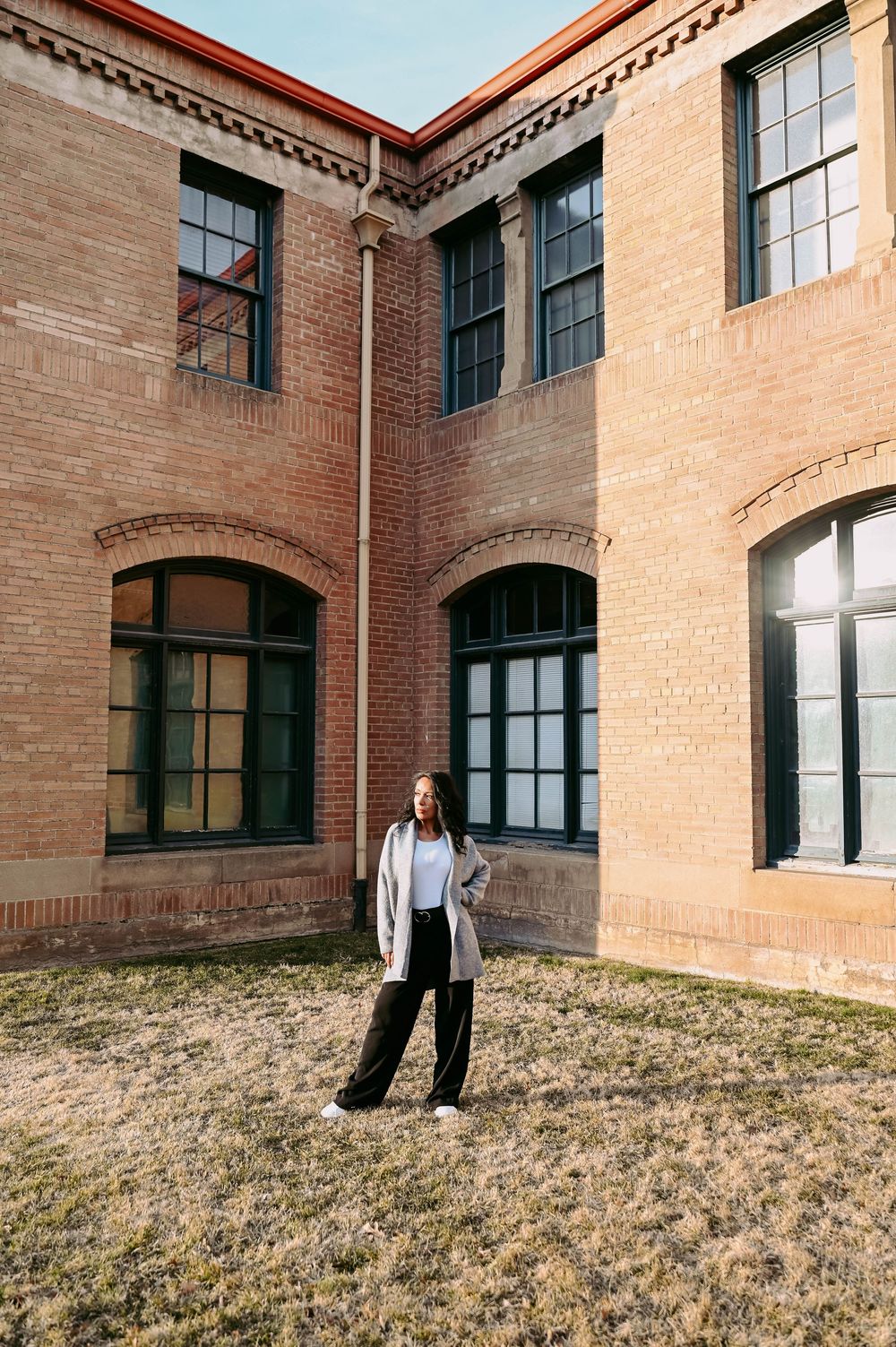 Fashion portrait against a historic brick building exterior with arched windows and architectural details.