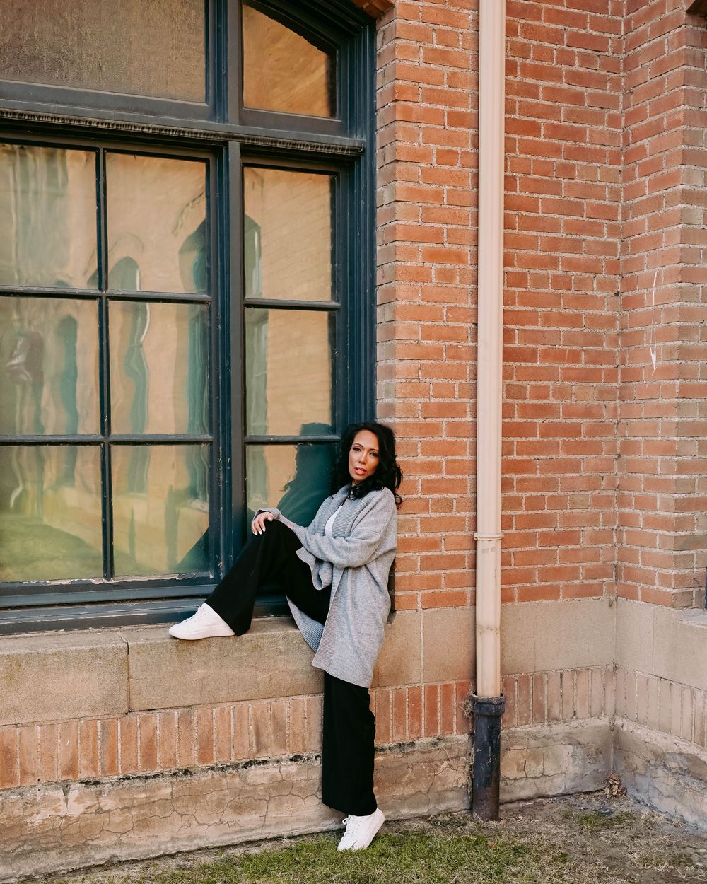 Urban fashion photography featuring casual wear against a historic brick building with large windows.