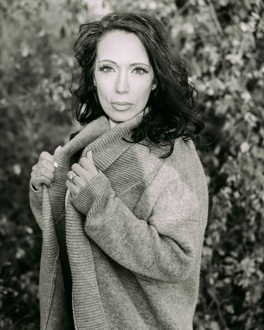 Black and white portrait in soft lighting featuring a cozy sweater and natural outdoor setting.