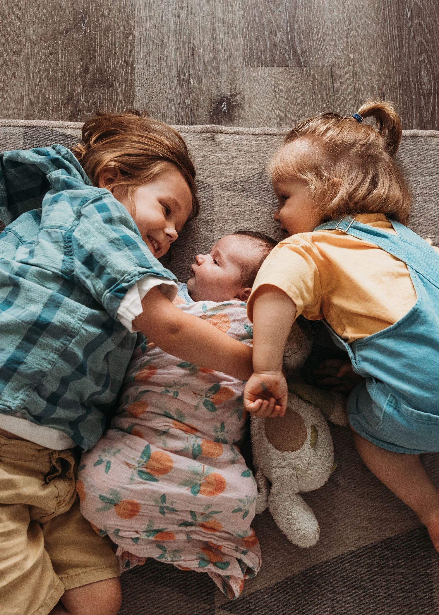 Three children laying on a cozy floor together, wearing casual clothing in teal, orange and floral print.