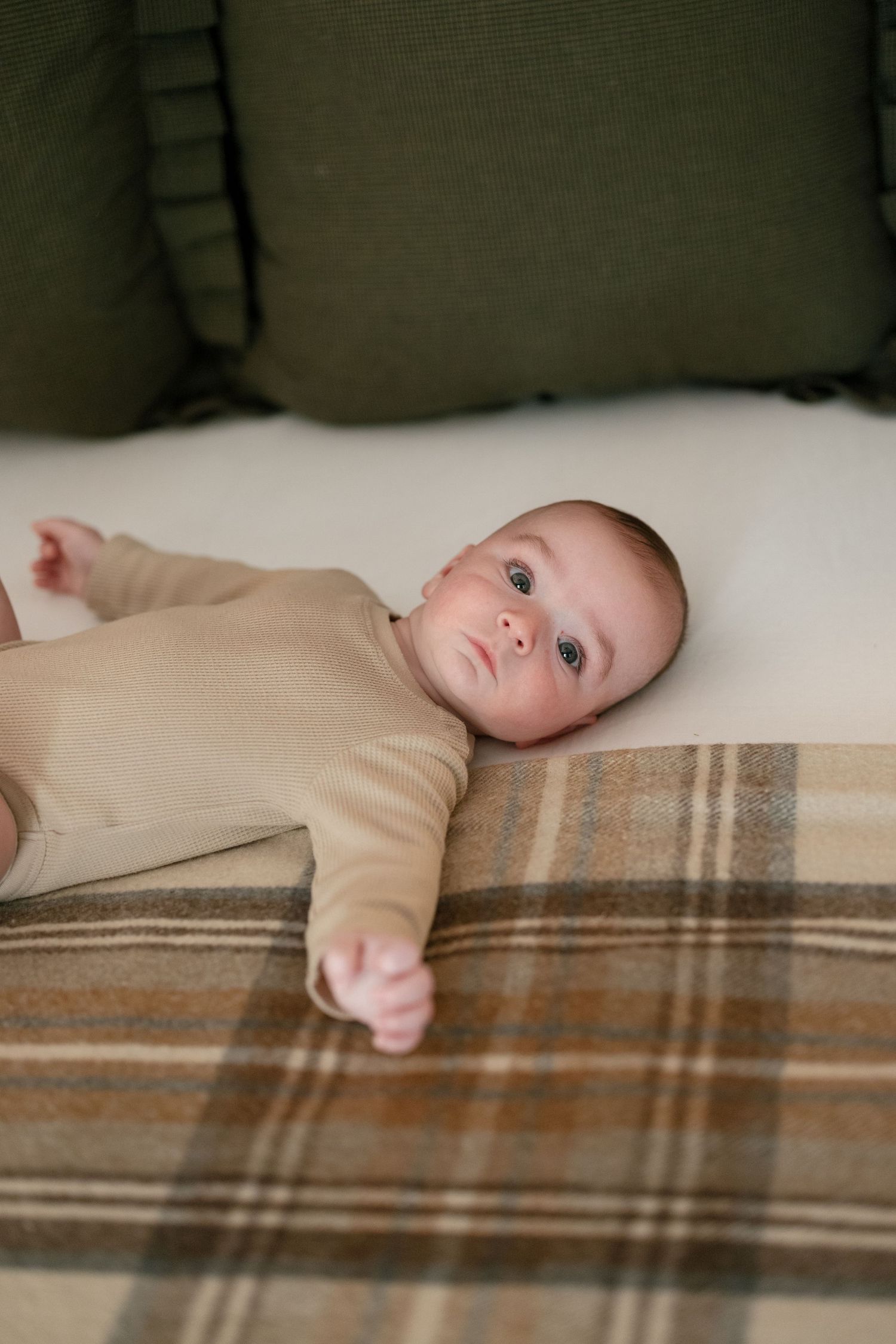 A baby lying on a beige and brown striped blanket in a series of connected images showing different head positions.