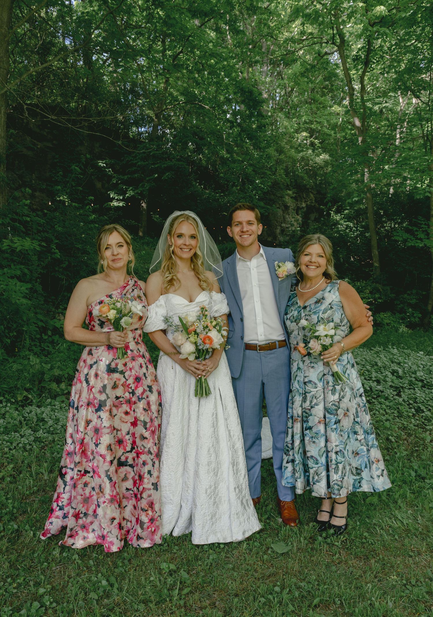 Wedding party poses for photos in a beautiful garden setting with floral dresses.