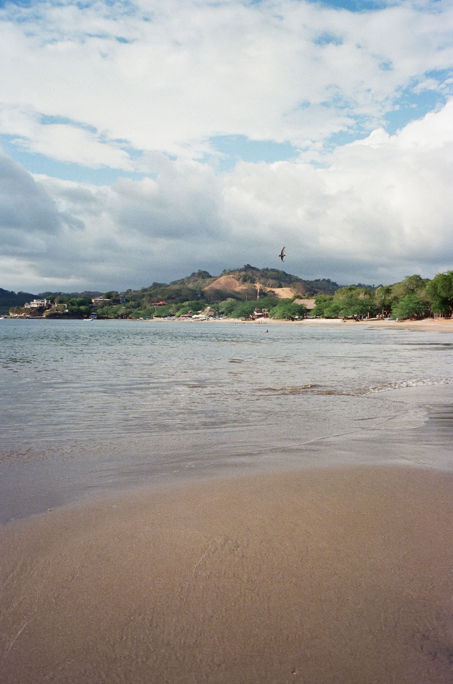 Panoramic view of a tropical beach with pristine sand and mountains in the distance under cloudy skies.