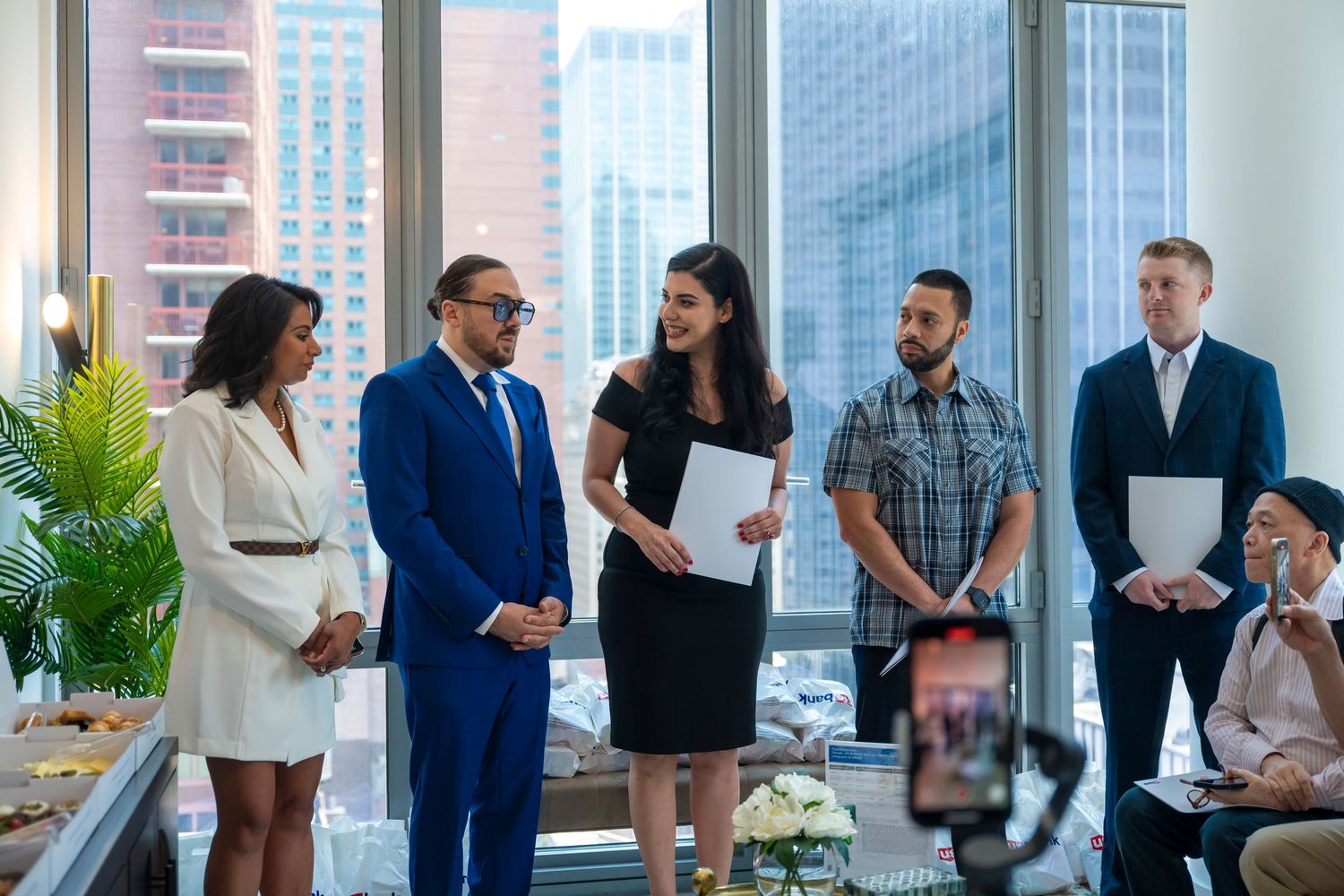 Business professionals gathered in a modern office space with city skyline views through large windows.