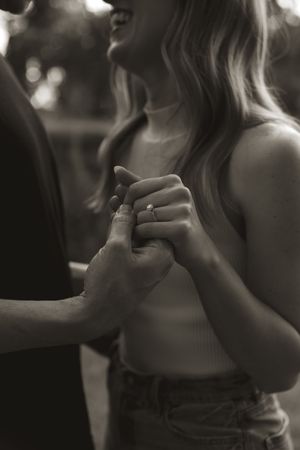 Black and white close-up of hands showing engagement ring in romantic moment.