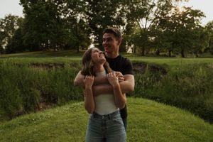 Couple enjoying tender moment together on grassy hillside at sunset.