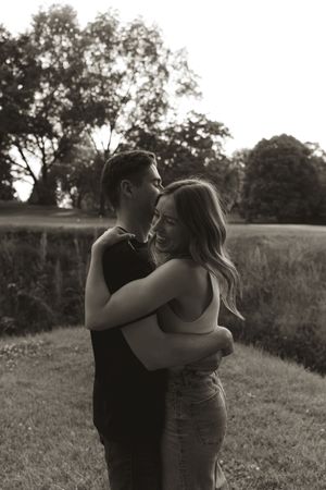 A black and white portrait of a couple embracing in a sunlit field.