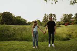 A couple holds hands while standing in a lush green field during golden hour.