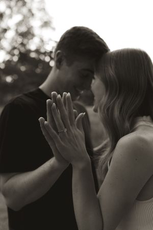 An intimate black and white photo showing clasped hands with an engagement ring.