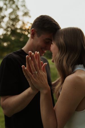 A couple shares a tender moment outdoors with hands raised to their faces.