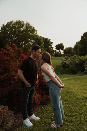 A couple stands together near blooming red bushes in a garden setting.