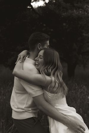 A tender embrace captured in monochrome photography against a natural outdoor backdrop.