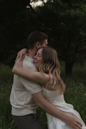Couple in matching white outfits sharing joyful embraces in a natural setting.