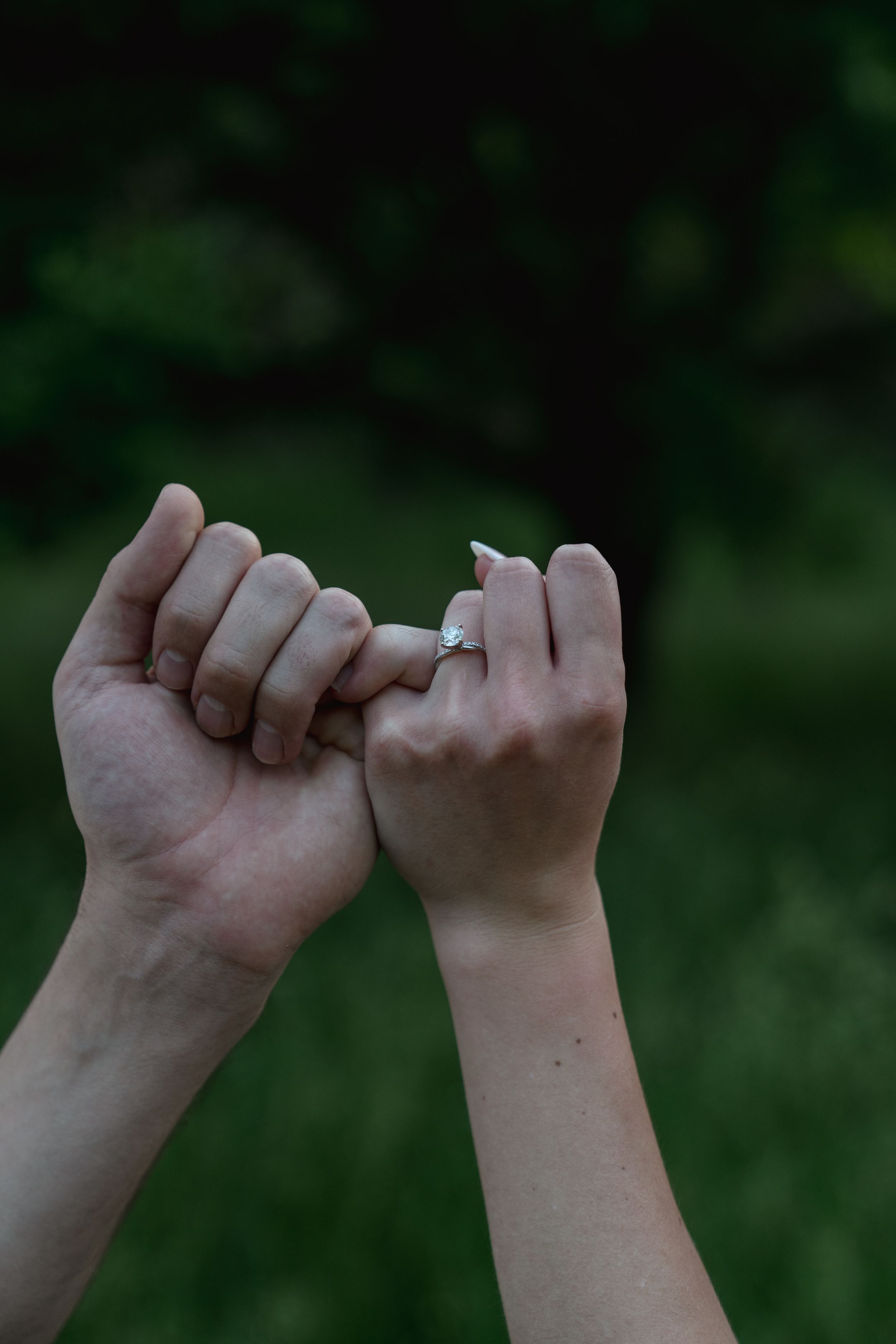 Close-up sequence of two hands making pinky promises against a blurred green background.