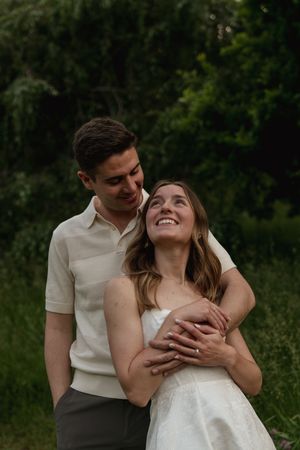 A couple shares a loving embrace while standing in a grassy field with trees in the background.