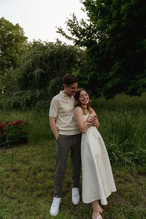 A couple in coordinated white and gray outfits shares a tender moment in a garden setting.