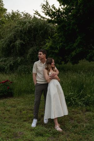 A couple embraces while standing in a natural garden setting during golden hour.