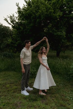 A couple dances playfully together in a garden with lush greenery.