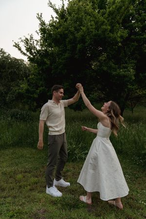 Playful couple dancing and twirling together in a meadow surrounded by trees.
