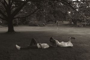 A couple relaxing on grass under a large tree in black and white photography.