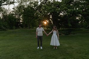 A couple walks hand in hand through a lush green park during golden hour.