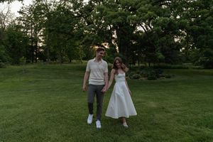 Two people stroll together on a grassy hill at sunset surrounded by trees.
